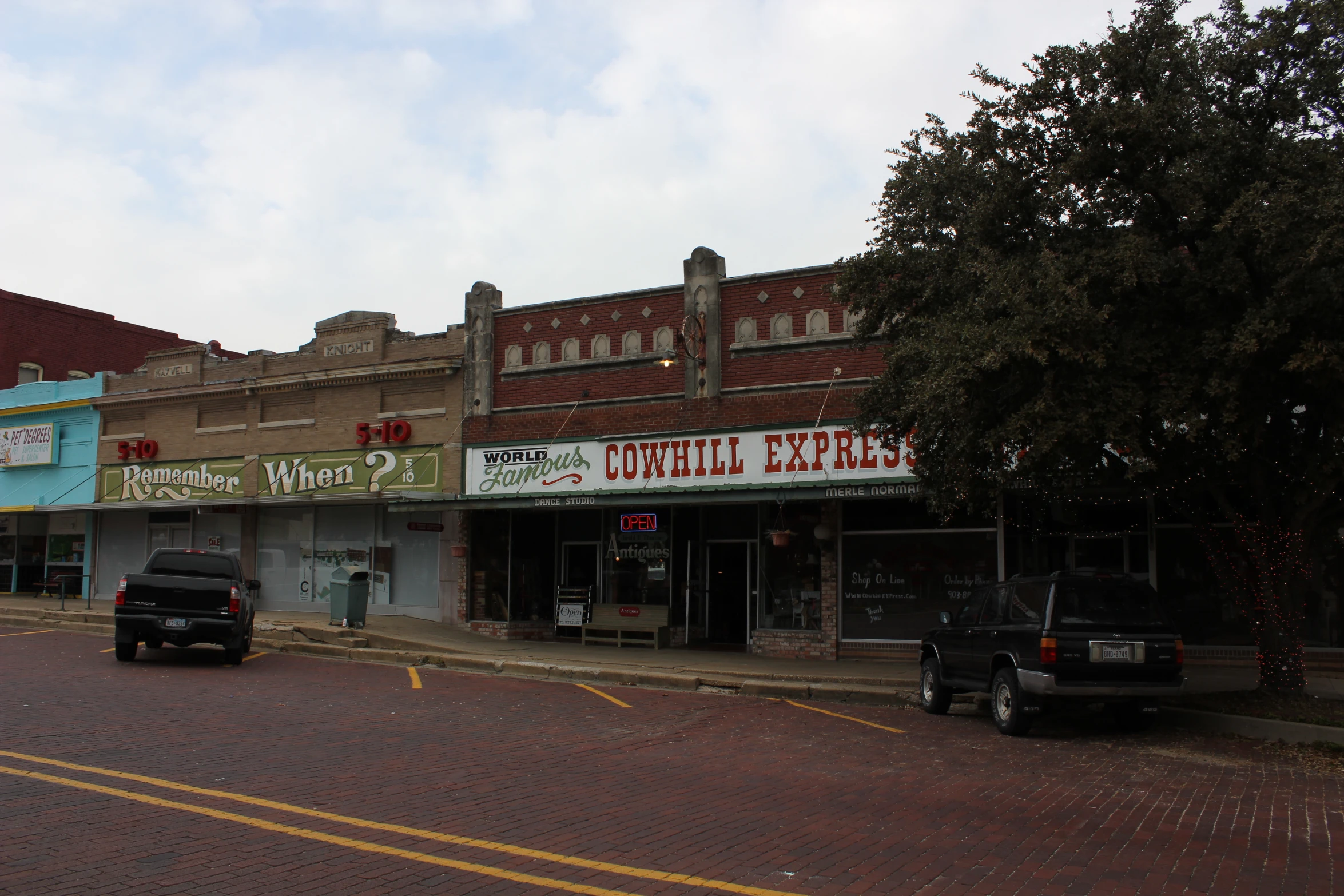 an empty street with shops on both sides and cars parked near by