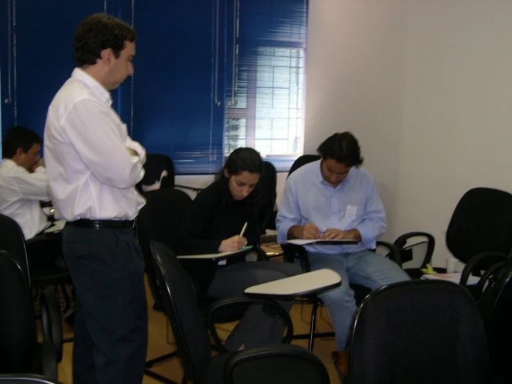 several people sitting in chairs and one person standing writing on paper