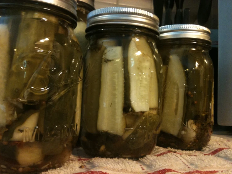 three jars full of pickles sitting on top of a cloth