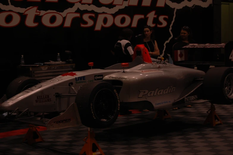 a grey race car sits on display in front of some men