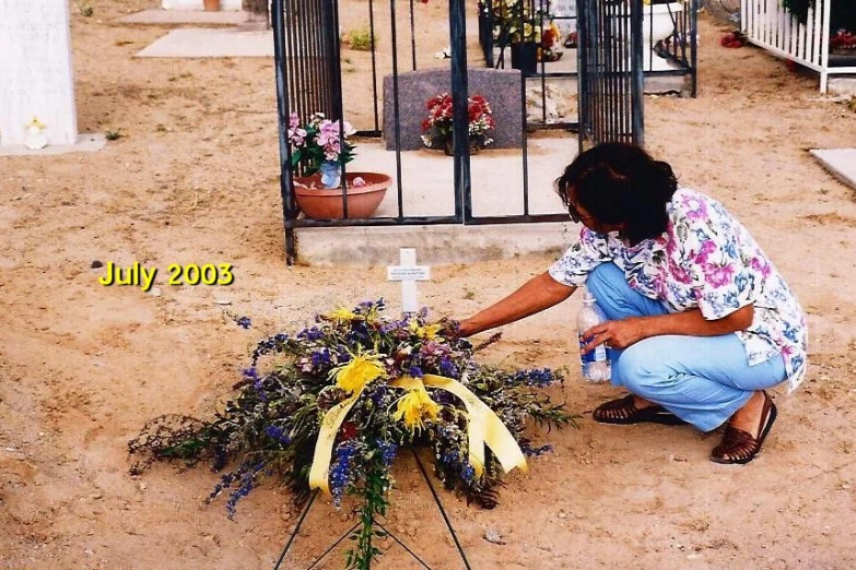 a person kneeling down with flowers in front of a grave