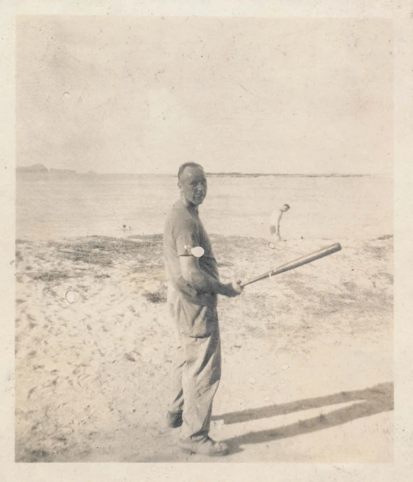 man holding a wooden bat on beach with birds flying nearby