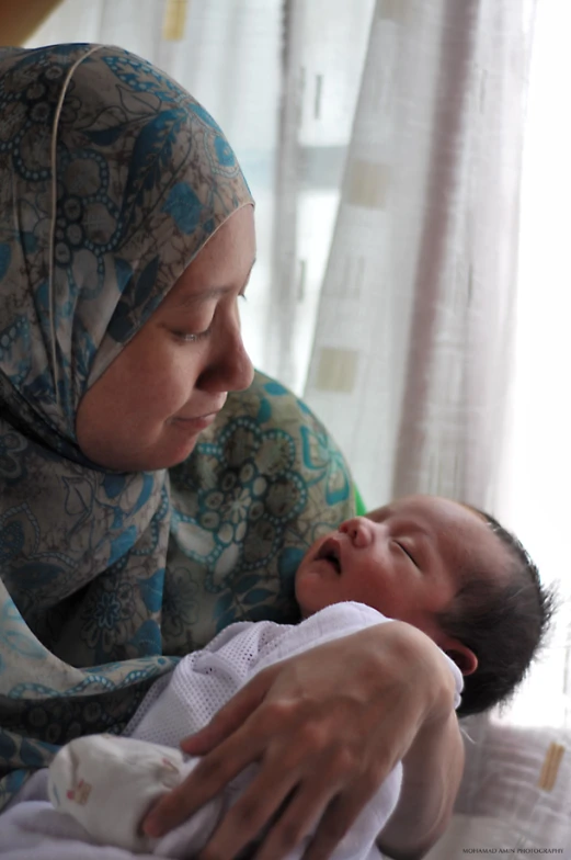 woman in hijab holding and looking down at a sleeping baby