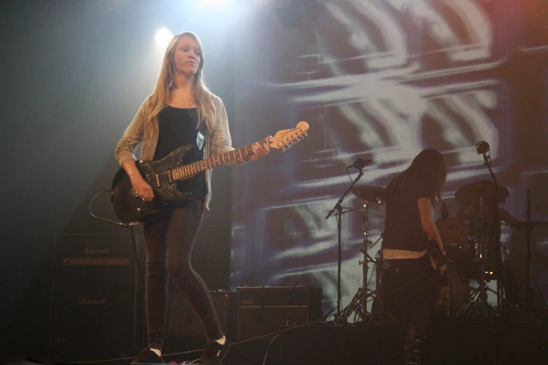 woman playing guitar at concert while another plays on bass