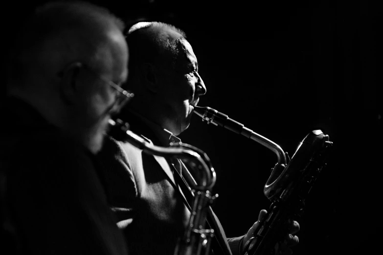 two men are playing trumpet on a dark stage
