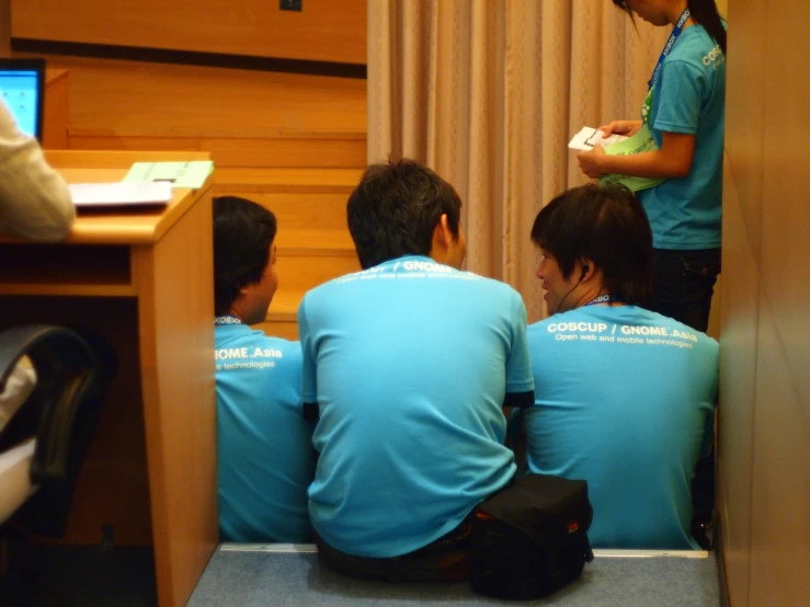 men in blue shirts sit around at a desk