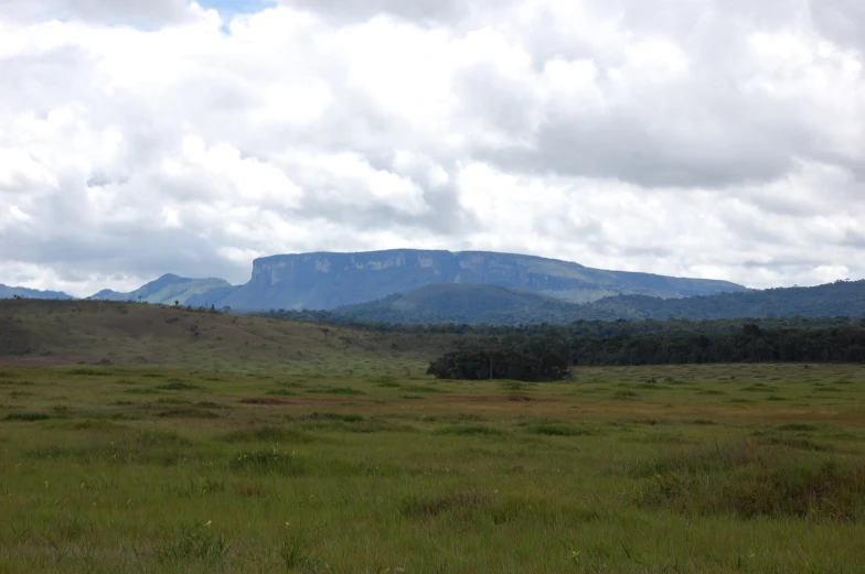 green grassy field and mountain range under cloudy sky