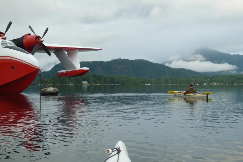 man in kayak near large airplane over calm body of water