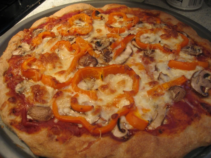 pizza with cheese, mushrooms, peppers and sauce sitting on metal tray