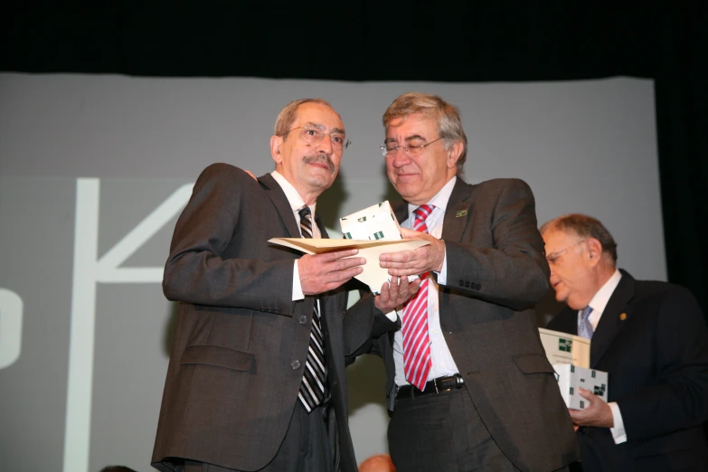 two older gentlemen hold papers while wearing suits