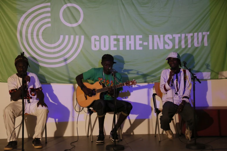 three men sing and play guitar while a man plays the guitar