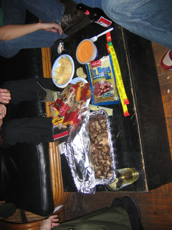 people sit on a wooden floor near food and drink