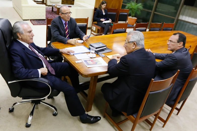 two men in business suits are sitting at a wooden table