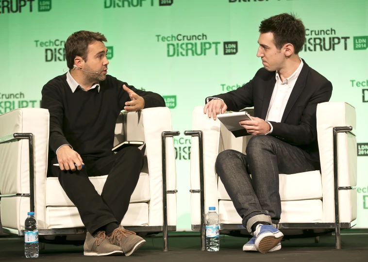 two men are seated on chairs discussing soing