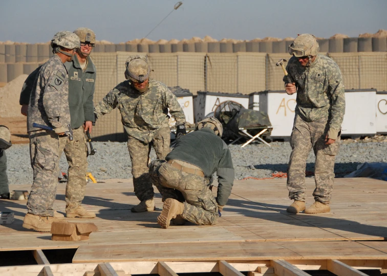 five people in army fatigues working on a wooden platform