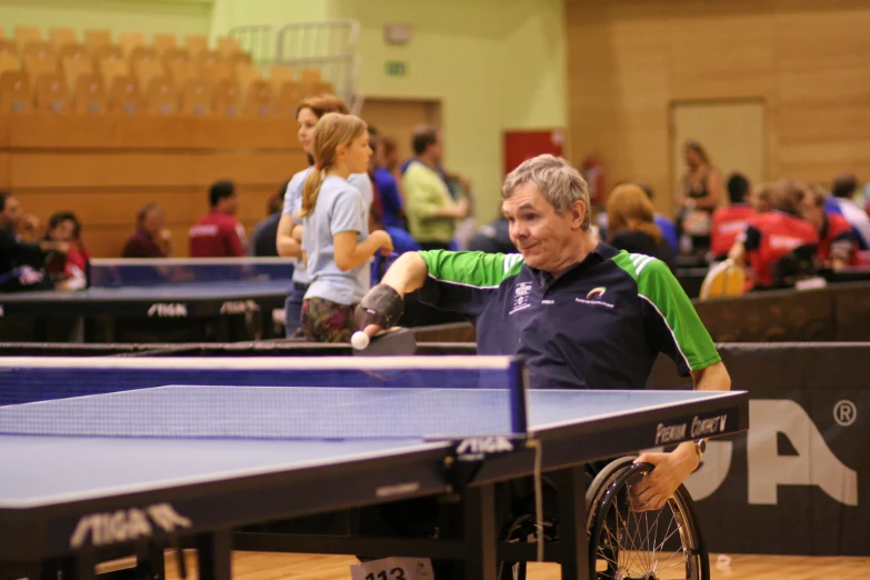 an old man playing table tennis in front of the audience