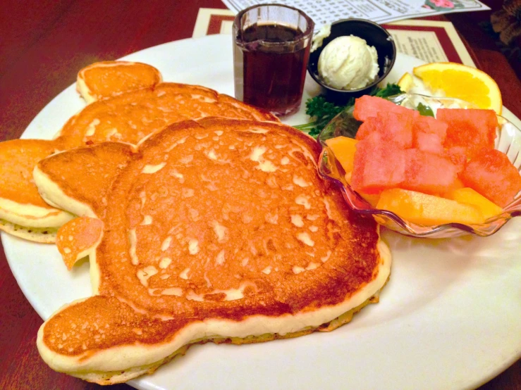 pancakes sit on a plate with fruit and cups