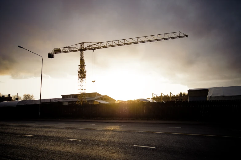 a crane stands in the distance as the sun shines behind it