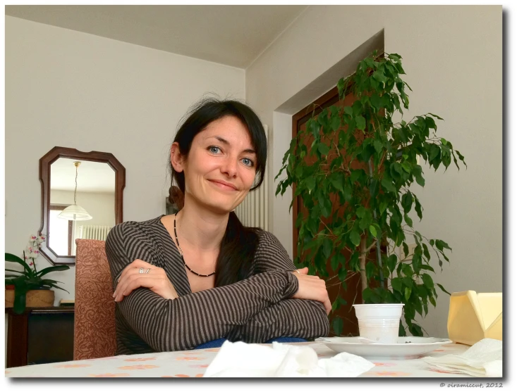 a woman sitting at a table with a mug and green plant