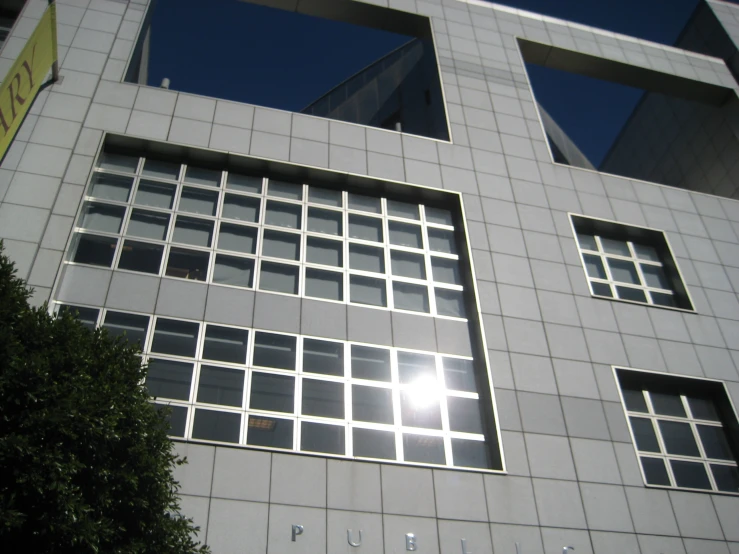 a gray office building with multiple windows and a green tree
