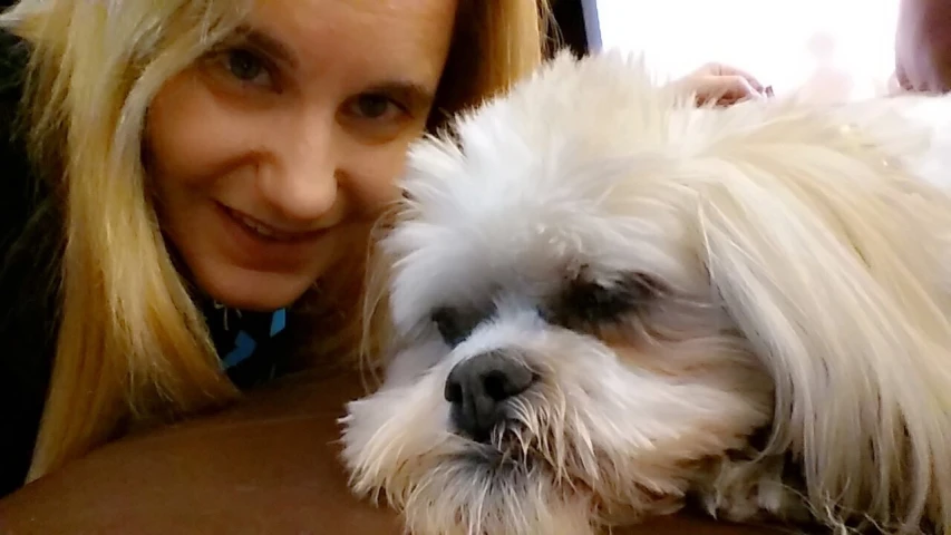 a woman with blond hair hugging a small white dog