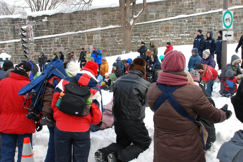 several people standing and sitting on the snow near a brick wall