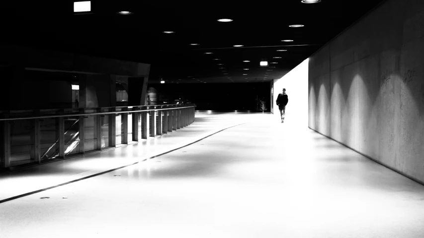 person walking down an empty hallway in black and white