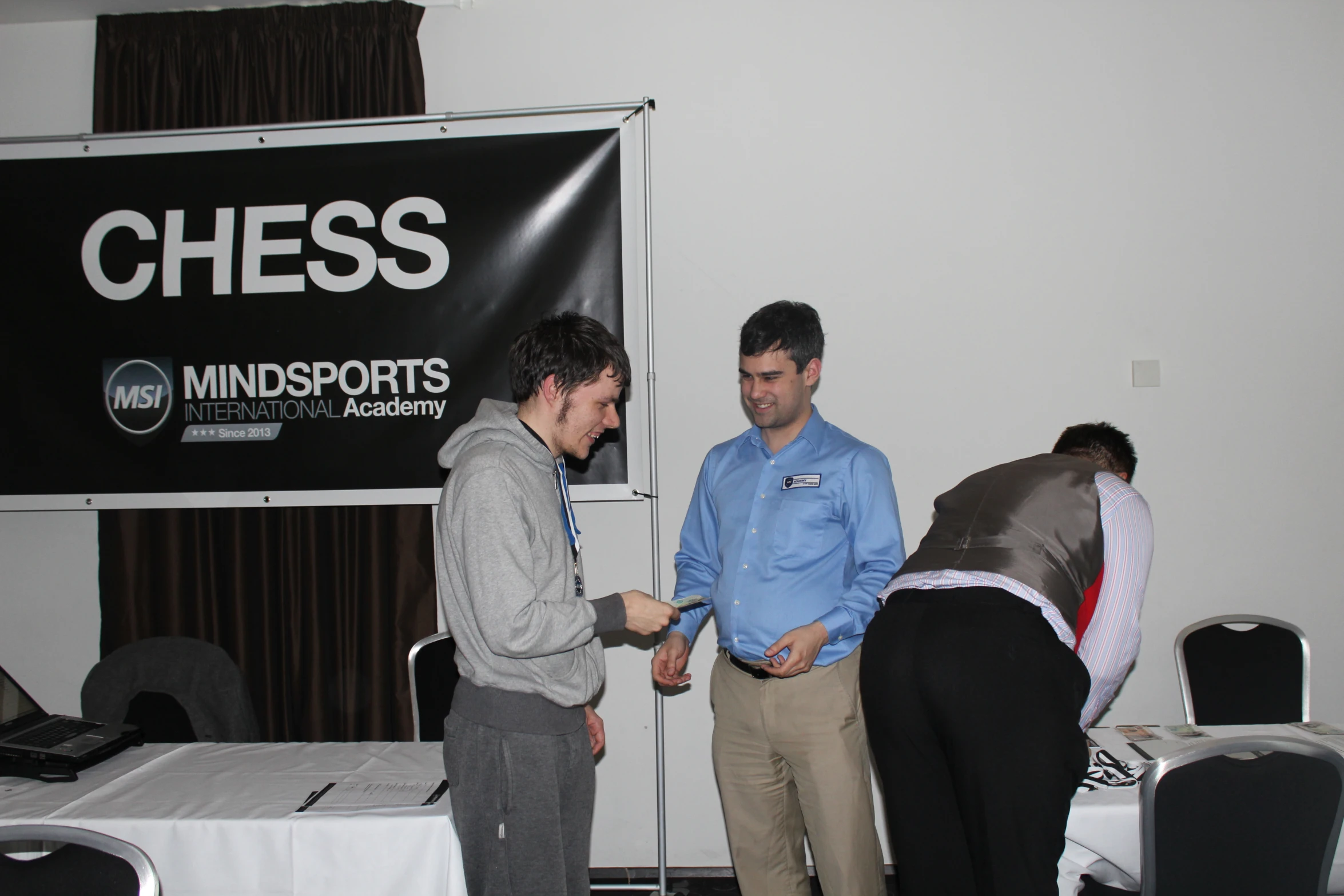 two men are standing at a podium while another man holds out a piece of paper to the other