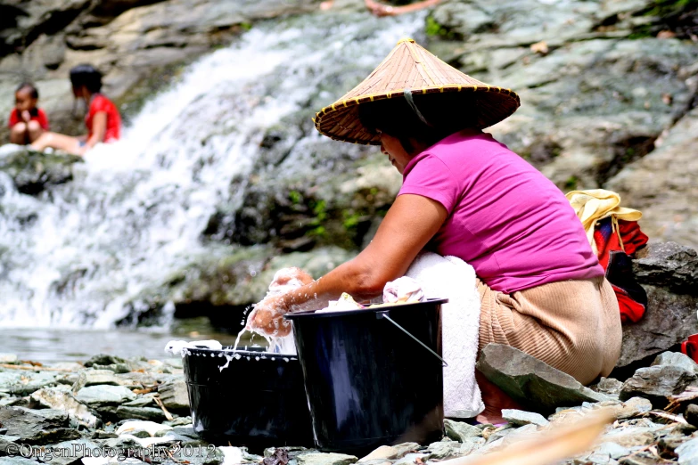 woman in a straw hat sitting by the stream of water