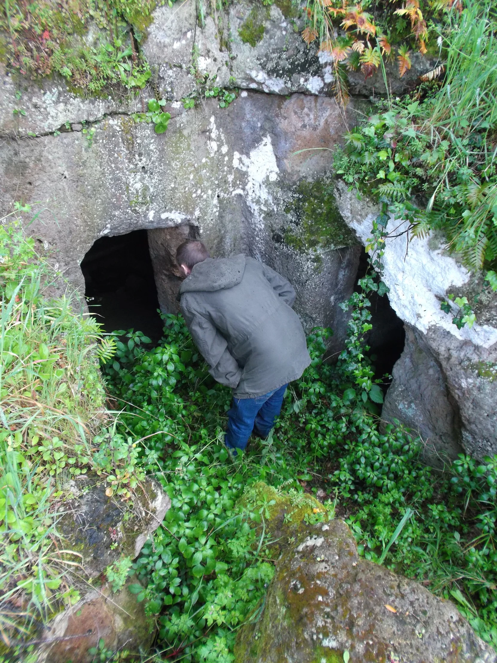 person standing at end of tunnel in large rock formation