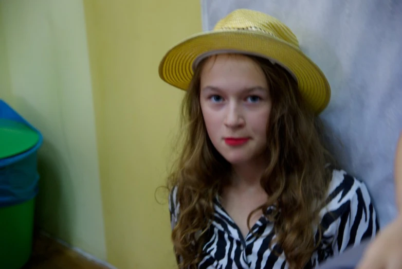 girl in yellow hat leaning on a wall