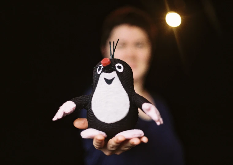 a person holding up a small penguin with a red nose