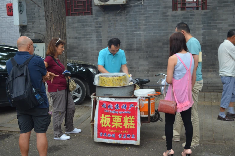 people gathered around a large yellow cake on a table