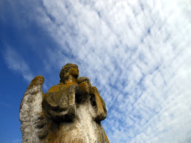 some kind of concrete angel on a hill top with a blue sky in the background