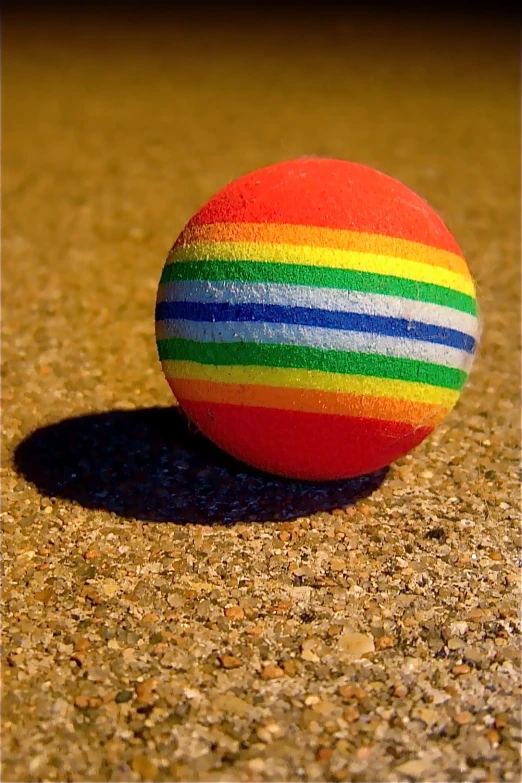 a brightly colored ball on a sidewalk with a shadow