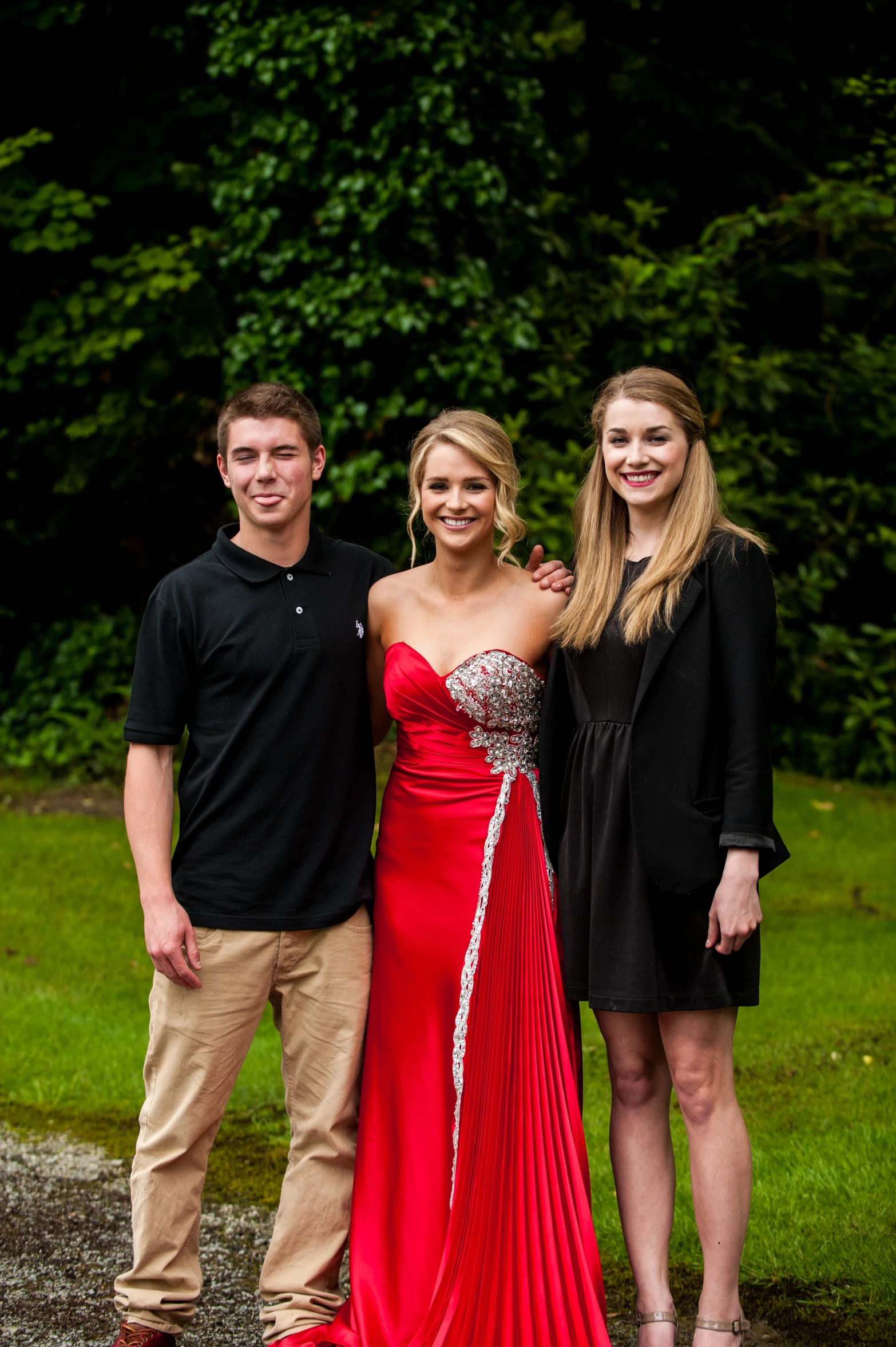 three people posing for the camera, one woman wearing a red dress