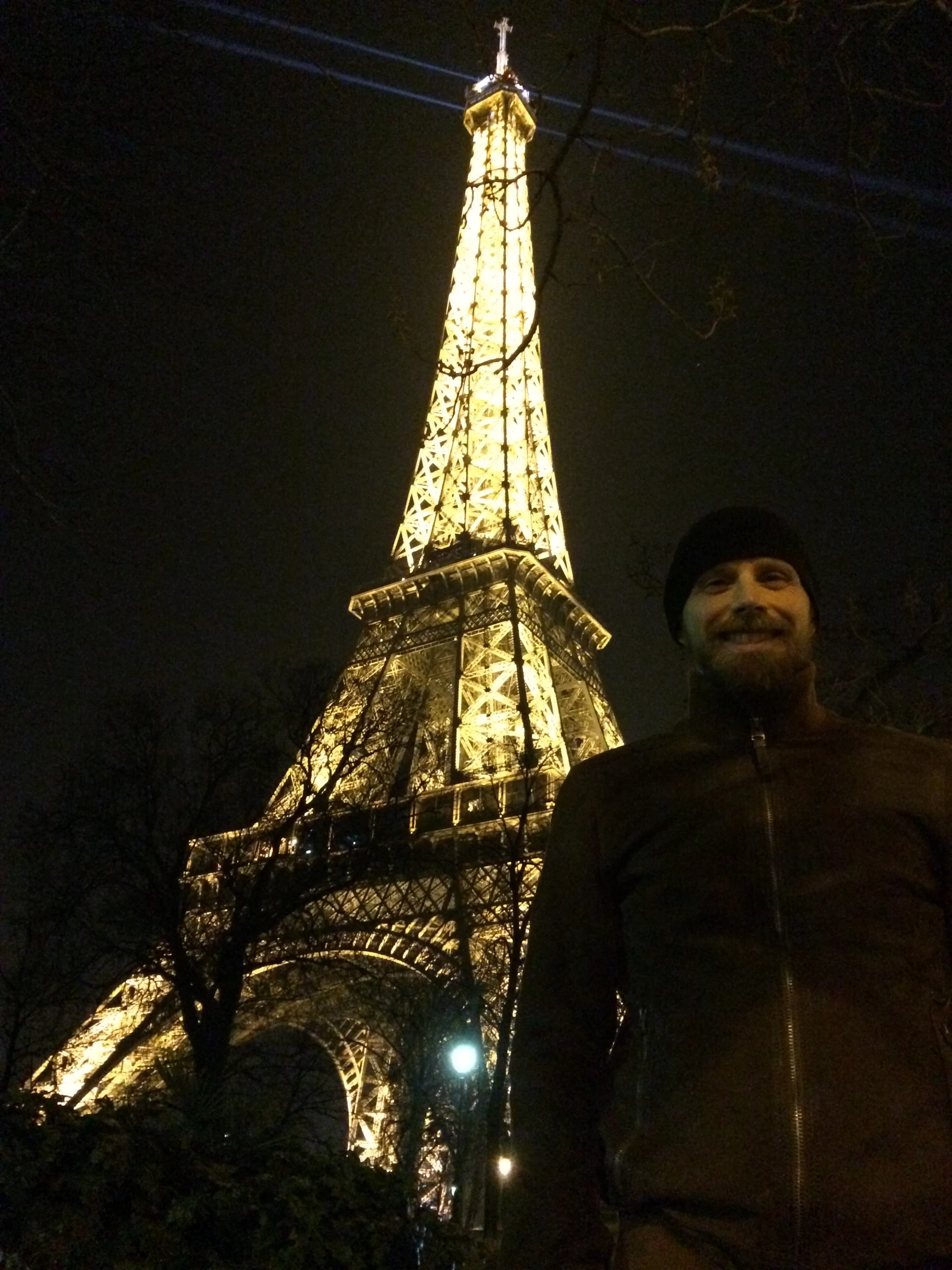 a man in a black top standing next to the eiffel tower at night