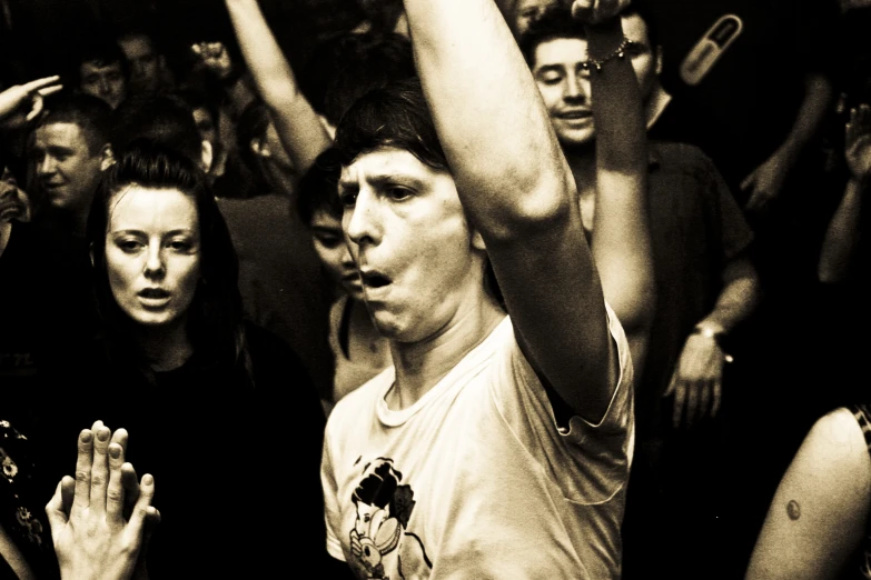 a man in a white t - shirt holds up his hand as people watch