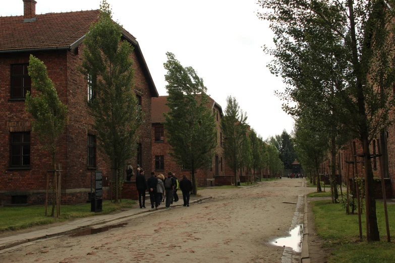 several people walking down a dirt road near some brick buildings