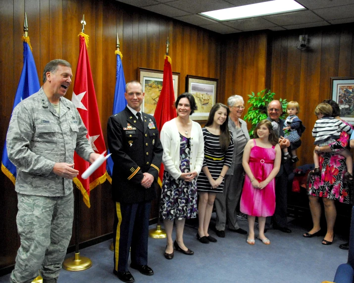 man in military uniform stands next to children and military men and women