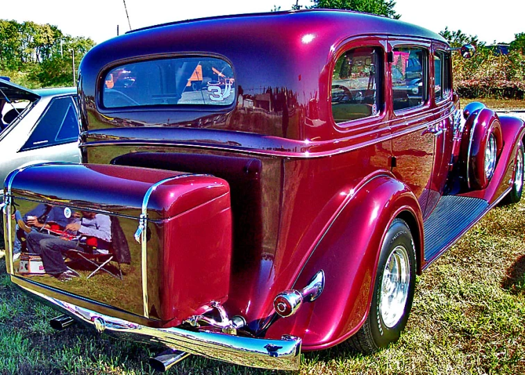 an old fashioned red car sitting in the grass