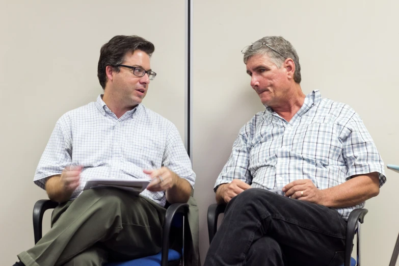 two men sitting in a chair talking and discussing