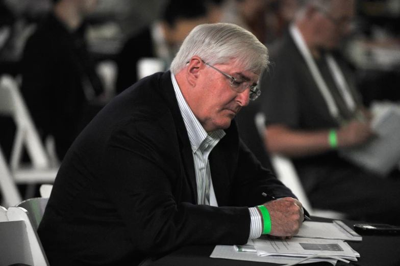 man wearing black suit sitting at table in conference