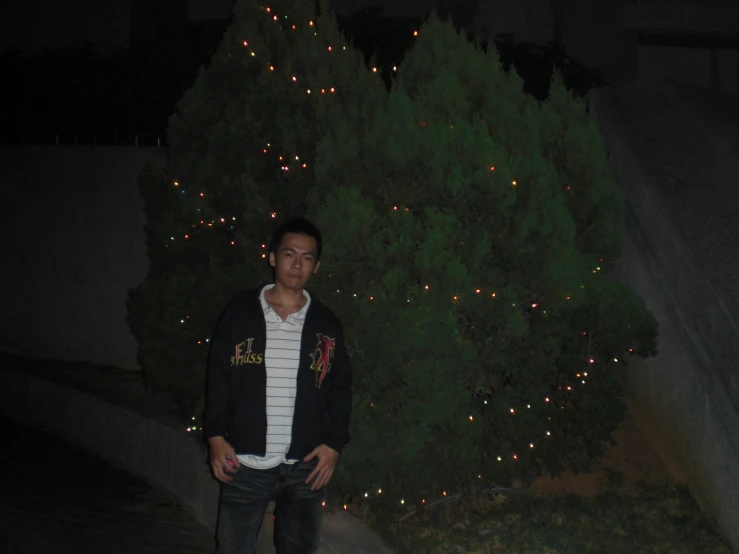 a man in a black jacket is standing near the christmas tree