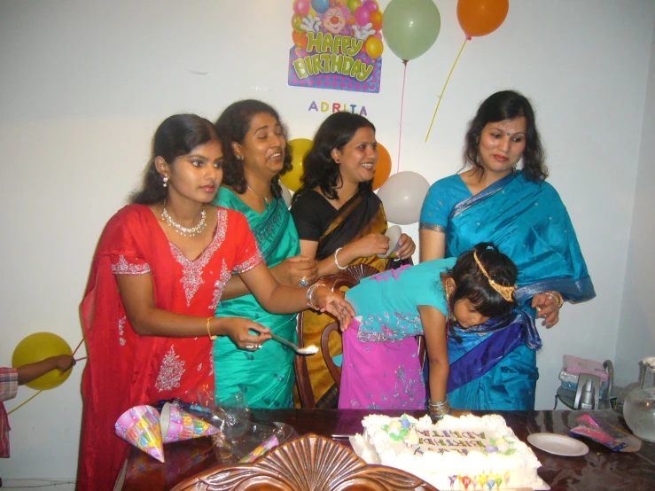 three woman are smiling while one of them has a cake