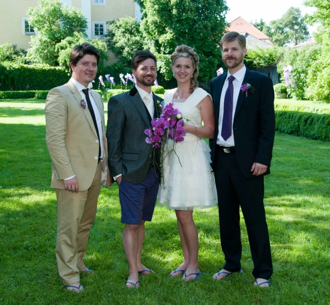 a bride and groom pose for a pograph with three people in formal attire