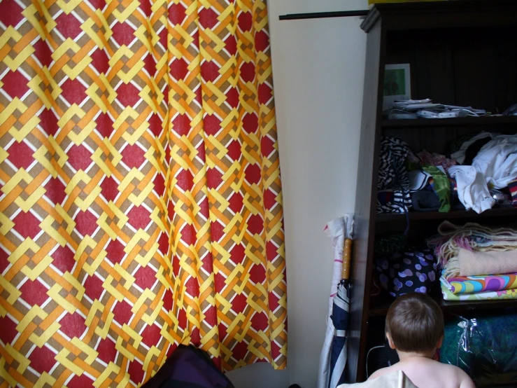 a boy stands by a window while looking at the curtains