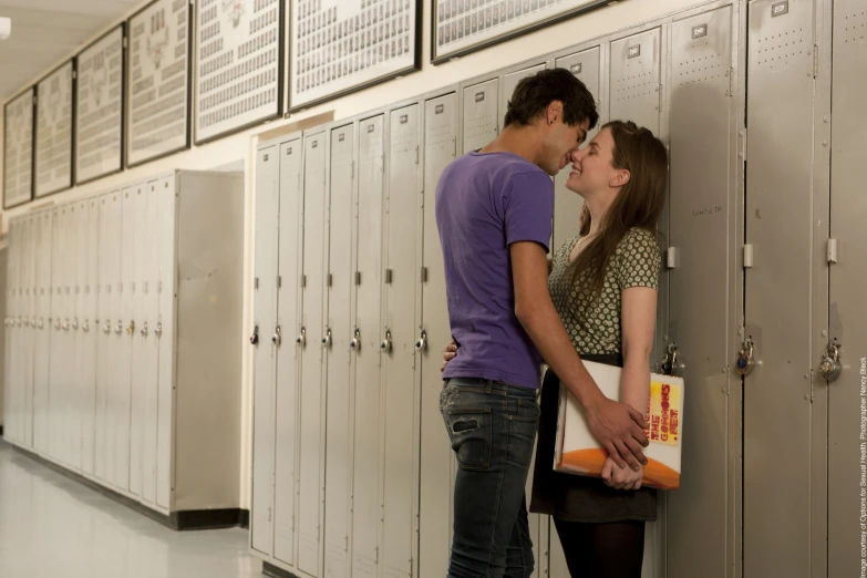 young couple kissing in lockers with binder for school