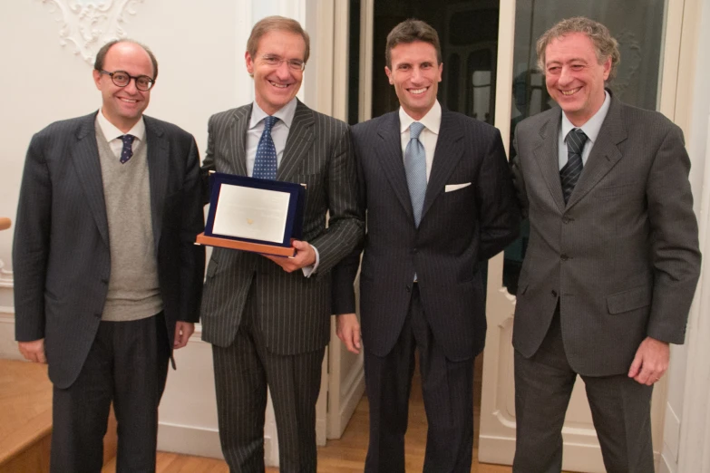 four men in suits standing on a wood floor posing for the camera