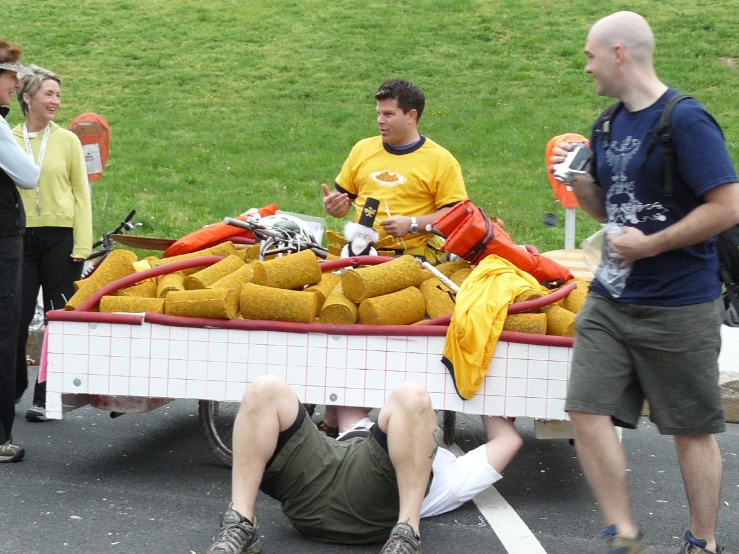 two men on a trailer with a woman nearby and a dog laying on the ground